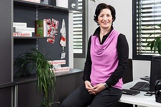 Mitarbeiterin IT bei STRABAG Foto von einer Frau im Büro, die auf der Tischkante sitzt und in die Kamera lächelt