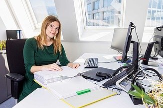 Bilanz Mitarbeiterin bei STRABAG Foto von einer Frau, die am Bürotisch sitzt und in die Kamera lächelt