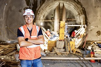 Erfahre mehr über die spannenden Herausforderungen im Ingenieurtiefbau Bauleiter Florian Fuchs steht mit Kladde und Helm auf einer Baustelle